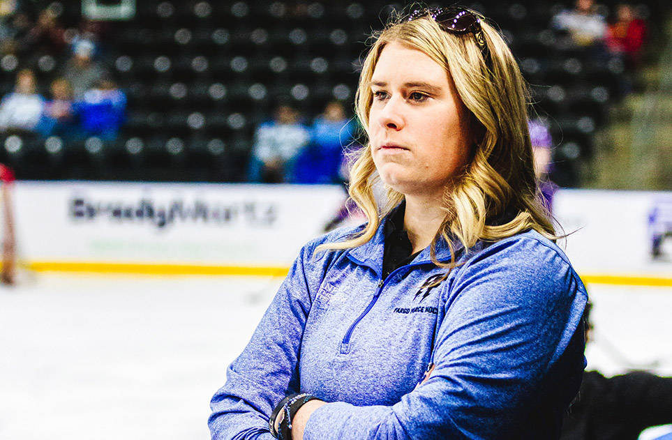 Lauren Rittle, wearing a blue Fargo Force hockey shirt, with the ice rink in the background.